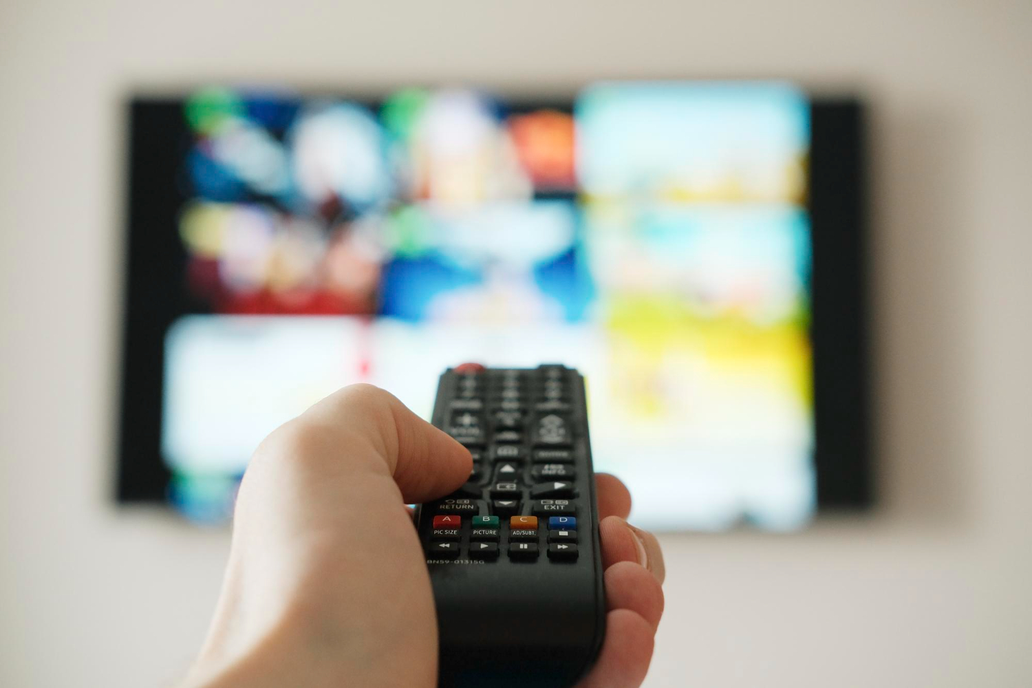 Bir adam uzaktan kumanda kullanarak televizyondaki kanalı değiştiriyor